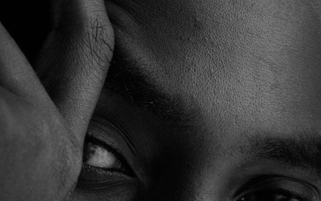 man staring into camera with hand partially covering his face